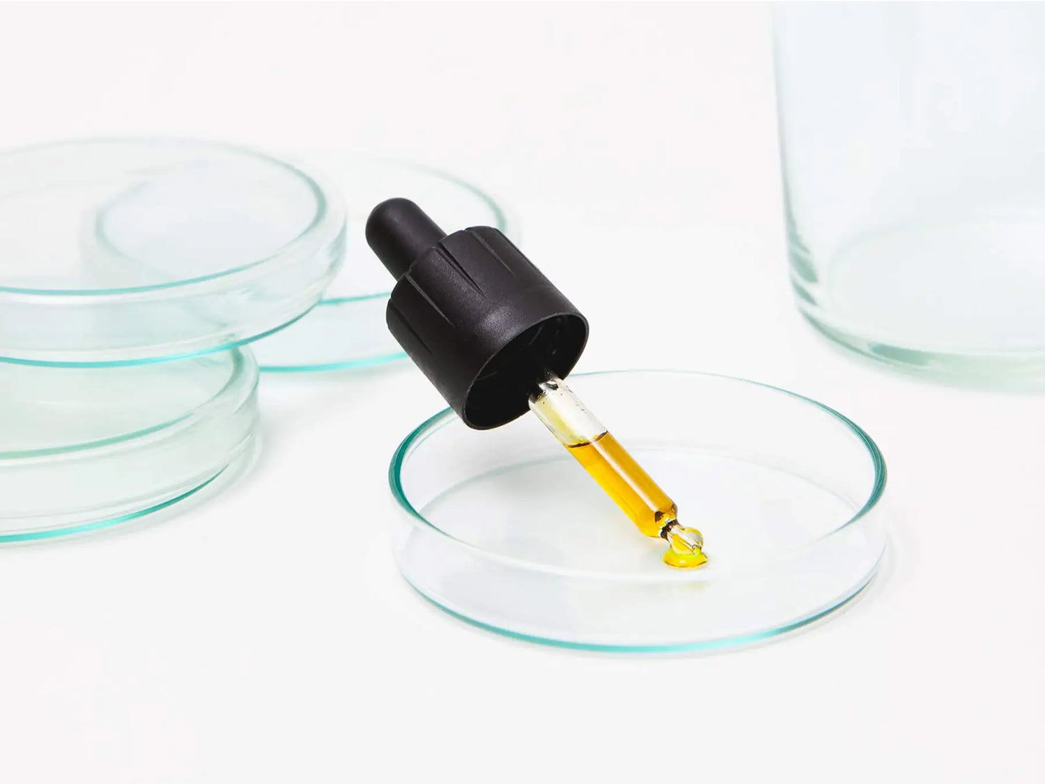 Pipette med gul olie dryppende ned i en Petri-skål i laboratorieindstilling.