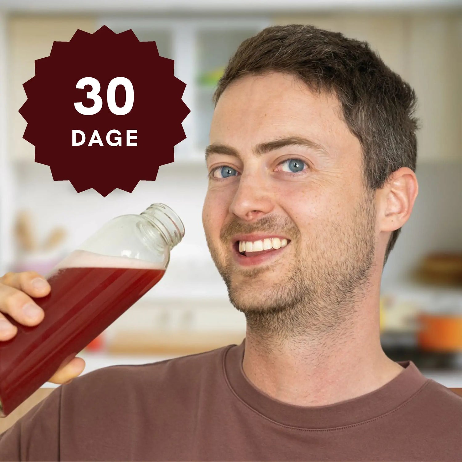 Mand i køkkenet holder en flaske med rød væske og smiler; 30 dage-badge