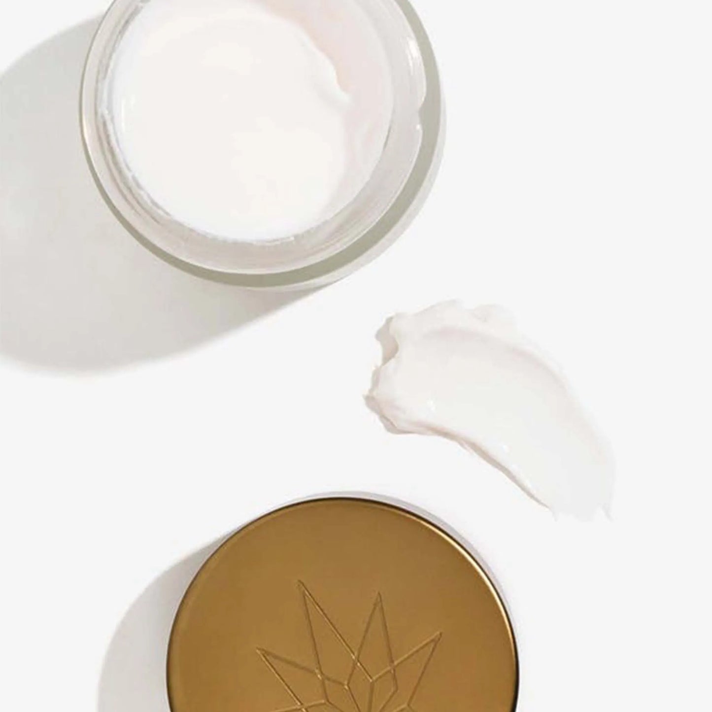 En åben pakke med CBD Natcreme + E Vitamin ligger ved siden af ​​låget og en klat creme.