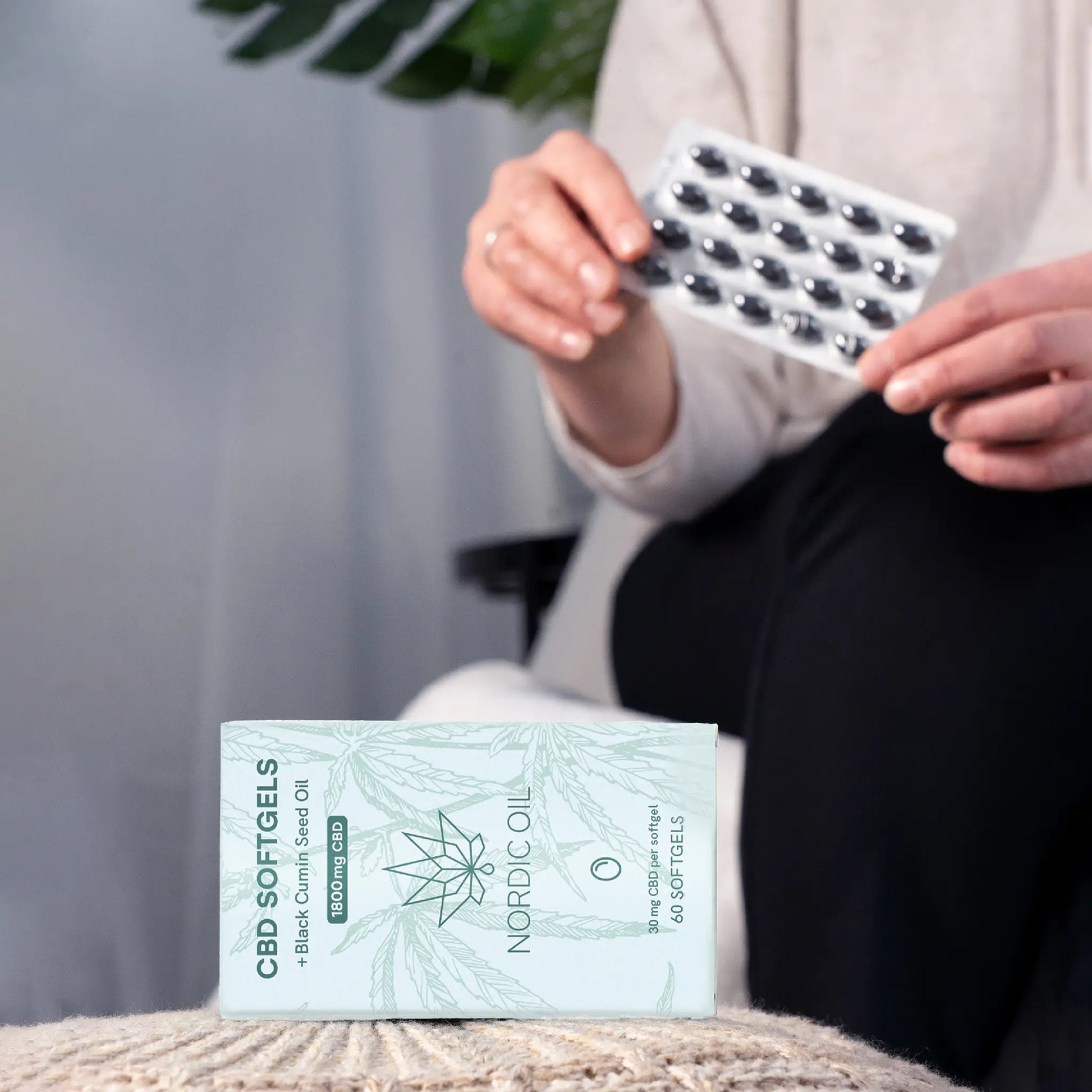 Person der holder en blisterpakke med CBD-softgels over en Nordic Oil CBD Softgels-æske.