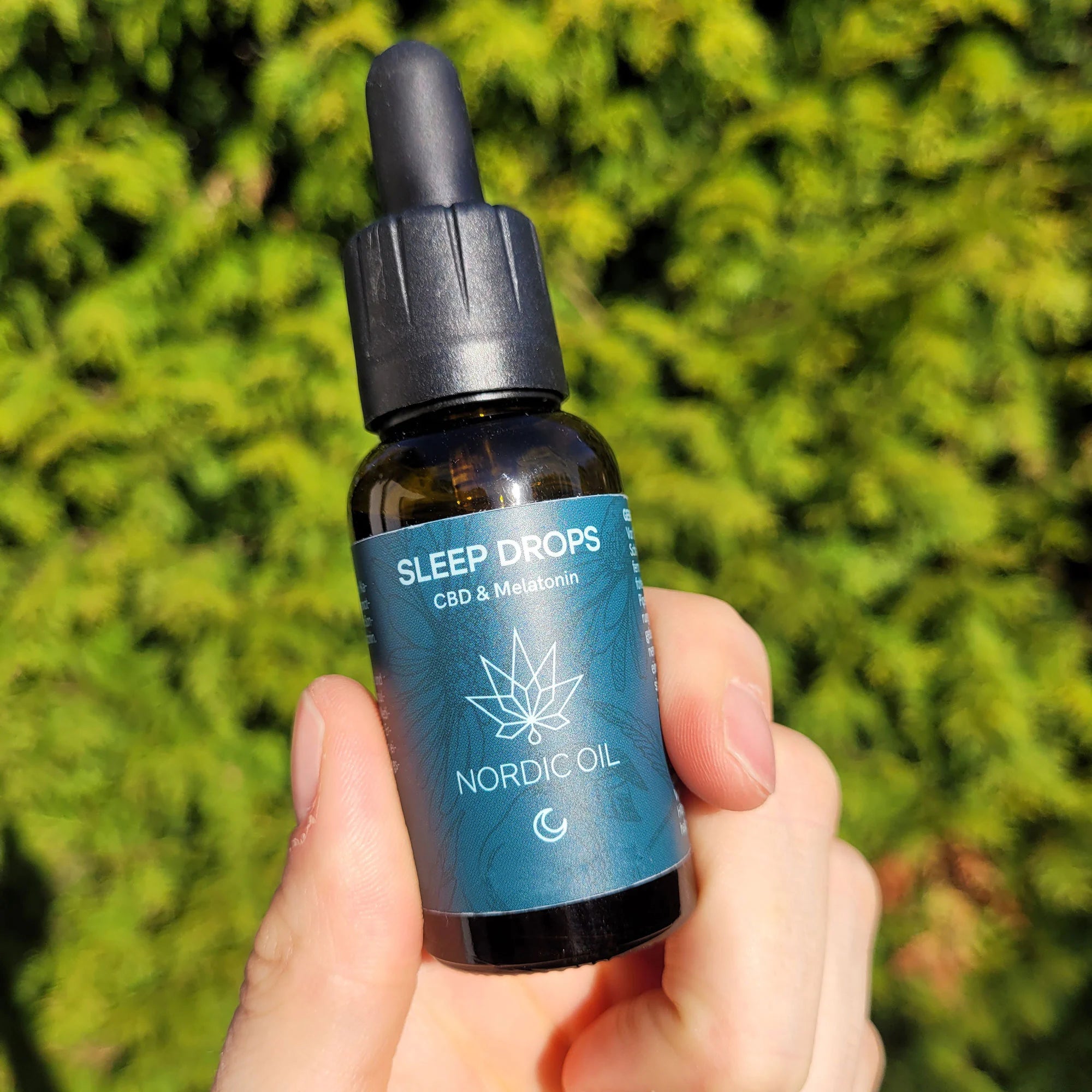 Nordic Oil Sleep Drops CBD og Melatonin-flaske med dropper foran grønne blade