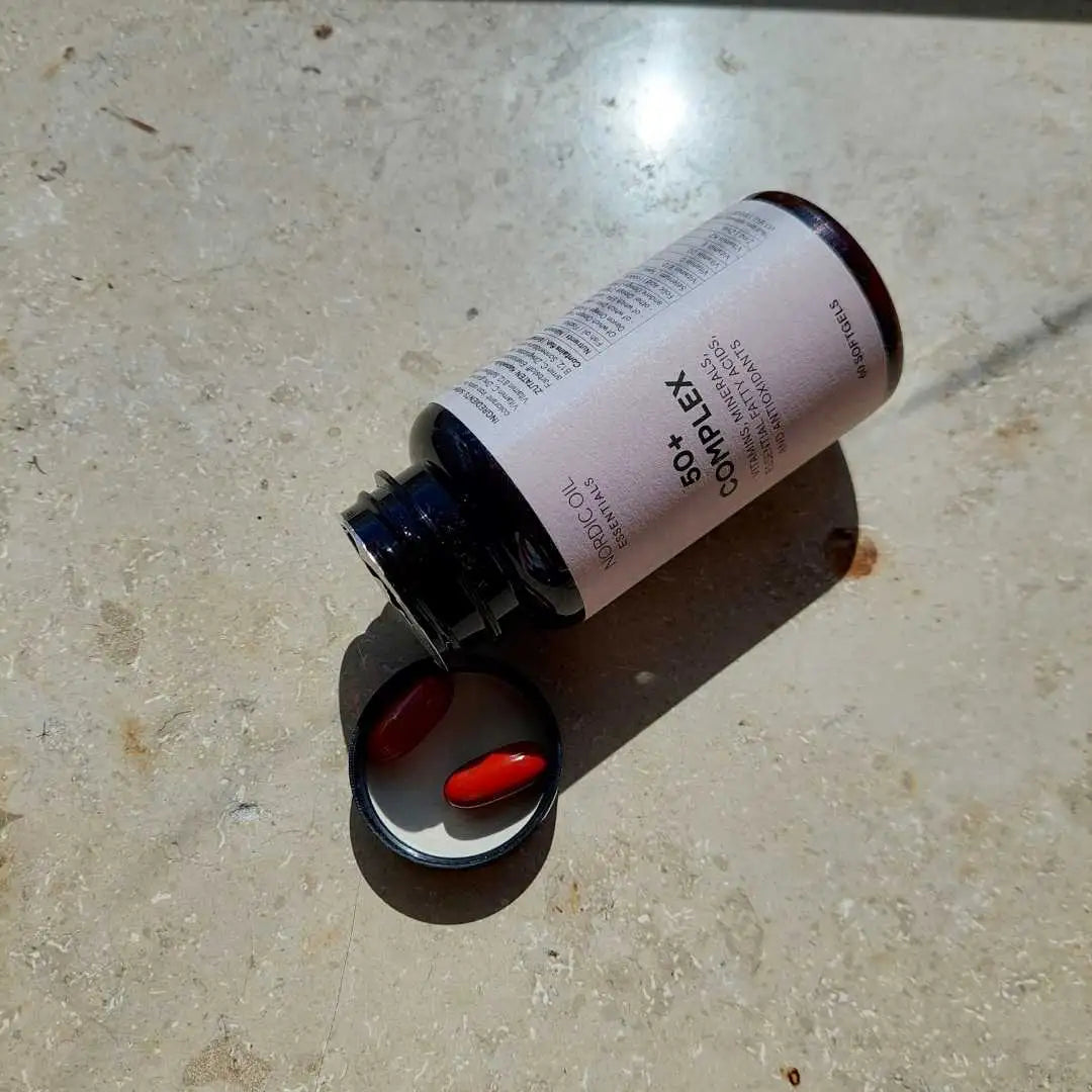 To røde CoQ10-kapsler ved siden af en åben flaske på en stenoverflade.