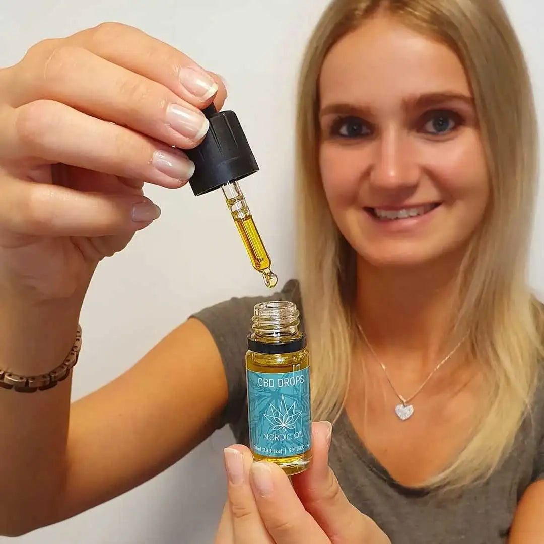 Kvinde viser en flaske CBD-dråber fra Nordic Oil med dropper.