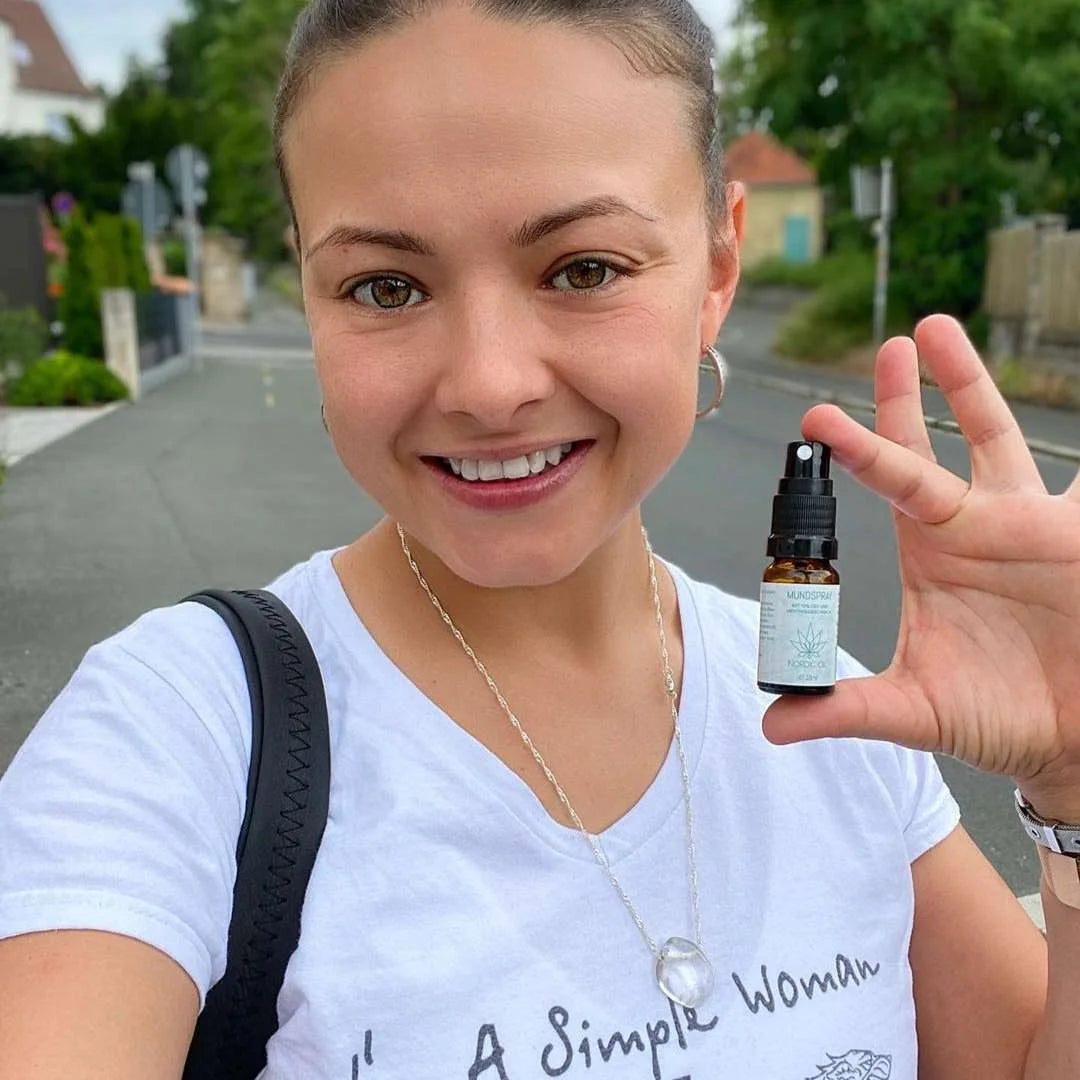 Smilende kvinde udenfor viser en lille sprayflaske med CBD-mundspray.