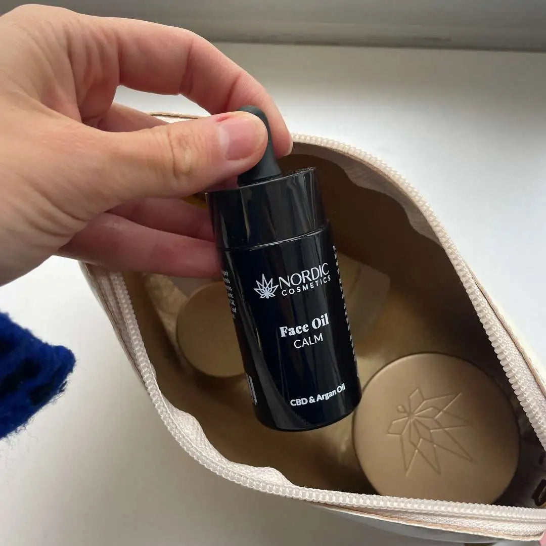 Hånd, der holder en flaske Nordic Cosmetics Face Oil Calm CBD & Argan Oil i en beige kosmetiktaske.