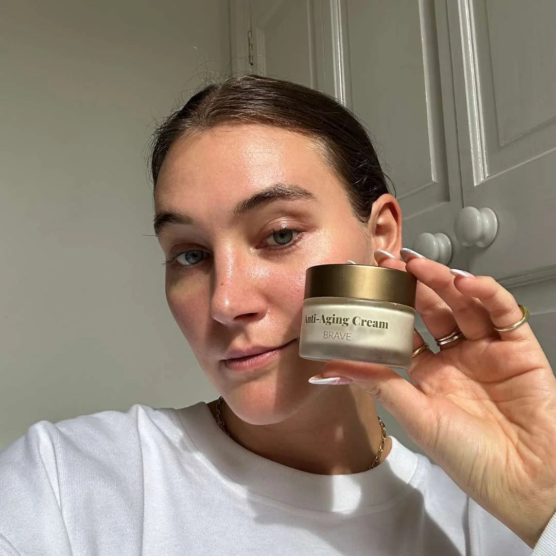 Kvinde viser en lille glaskrukke med anti-aging creme og gyldent låg.