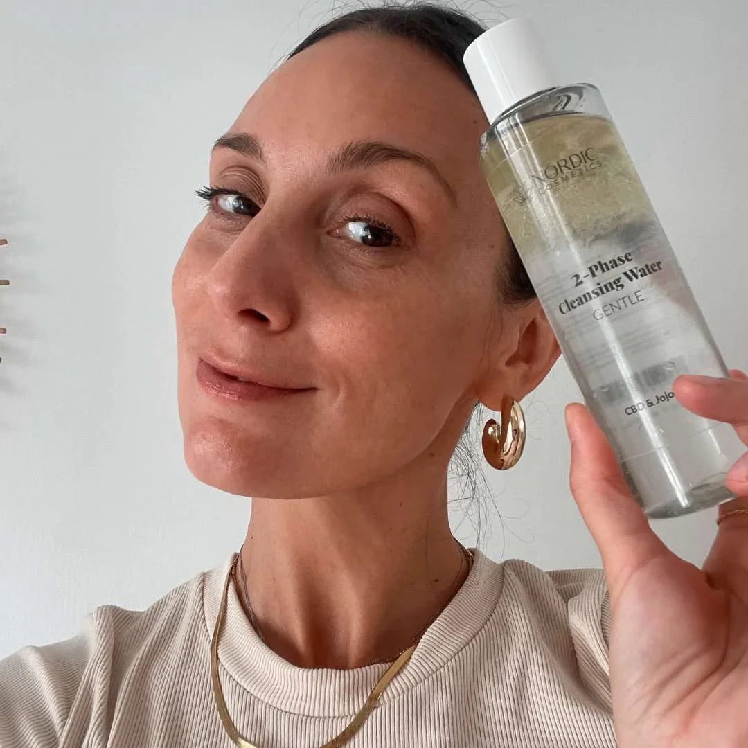 Kvinde holder en flaske Nordic Oil 2-Phase Cleansing Water tæt ved ansigtet.