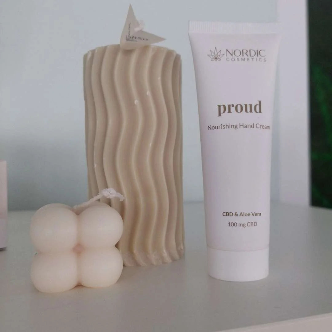 Nærbillede af Nordic Cosmetics Proud håndcreme med CBD og Aloe Vera ved siden af et bølget beige lys.