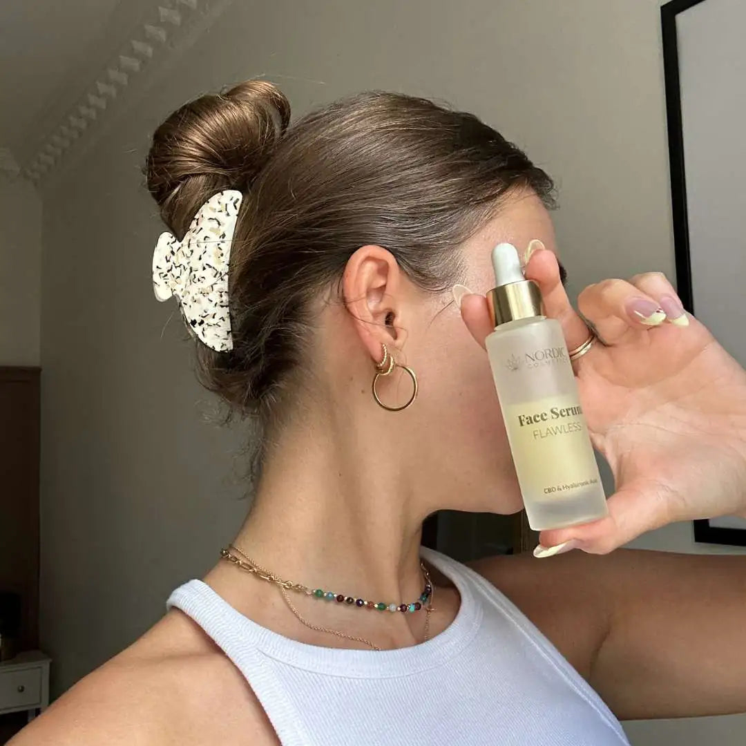 Kvinde holder Nordic Oil Face Serum Flawless-flaske med dropper foran ansigtet.