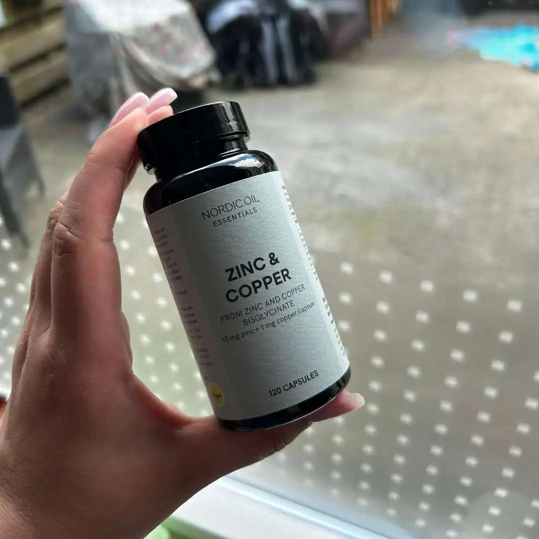 Hånd holder flaske med Nordic Oil Essentials Zinc & Copper kosttilskud i kapsler.