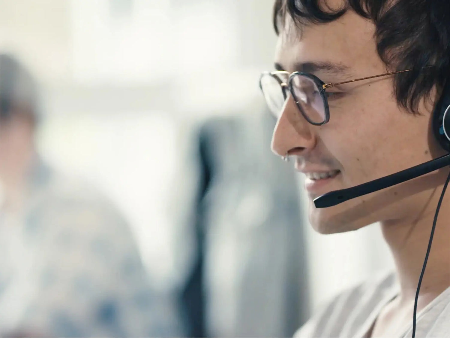 Kundeservicemedarbejder i profil med headset og briller i kontormiljø.
