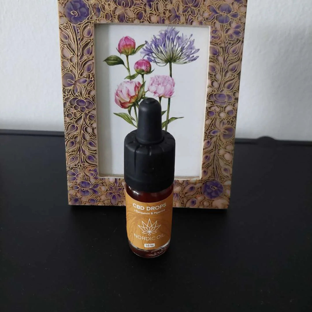 CBD-drops flaske fra Nordic Oil foran blomsterramme.