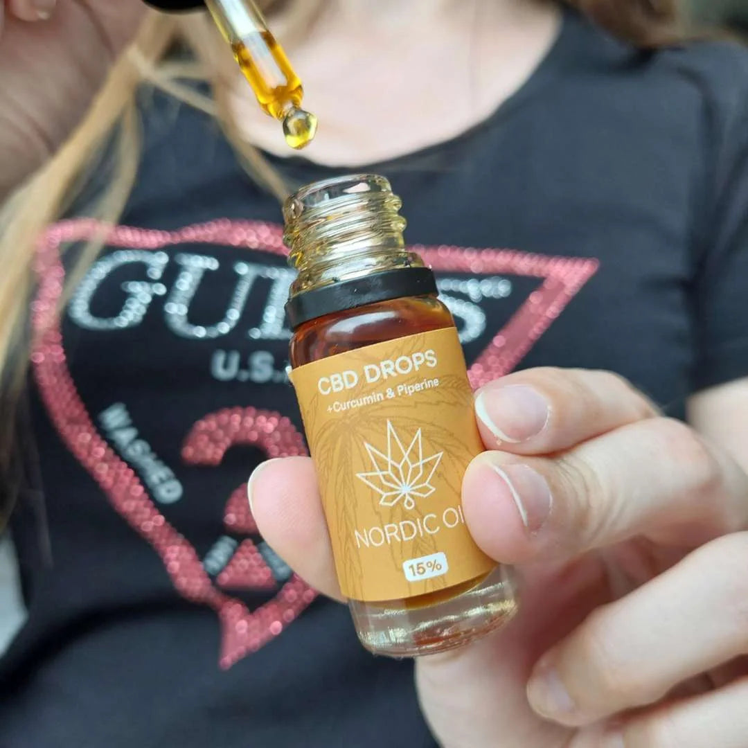 Nærbillede af en hånd, der holder en brun glasflaske med CBD Drops Nordic Oil og en pipette, der drypper olie.