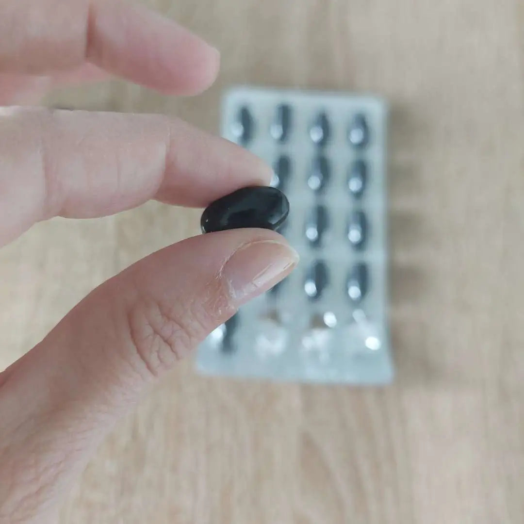 En sort kapsel holdes mellem fingrene, med en blisterpakke af kapsler i baggrunden.