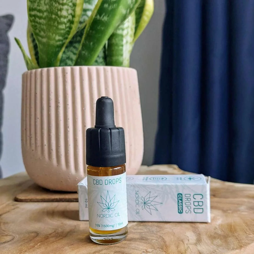 Nordic Oil CBD-dråber i glasflaske med dropper ved siden af æske på træbord, plante i baggrunden.