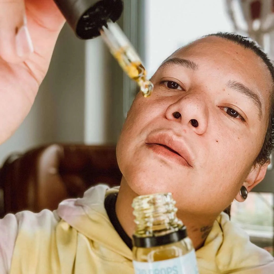 Mand med dropper der hælder CBD-olie fra glasflaske tæt på ansigtet