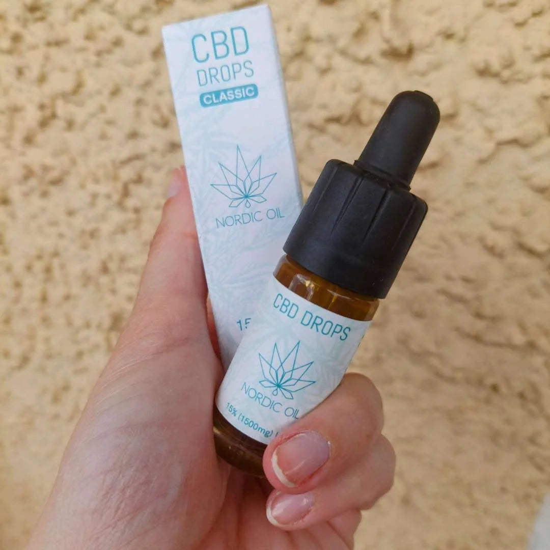 CBD Drops Classic Nordic Oil – lille brun glasflaske med dropper og blå etikette, holdt af hånd ved siden af æske.