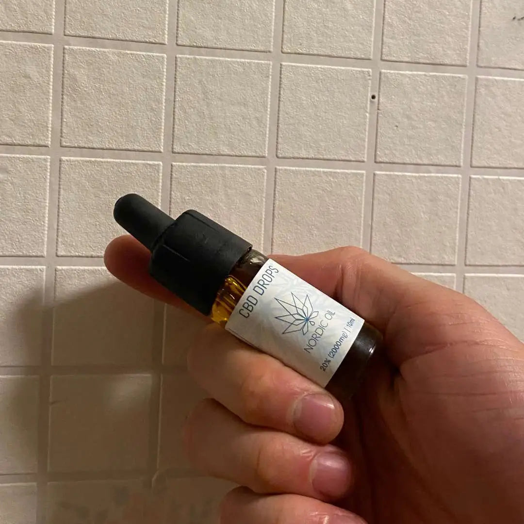 Lille mørk amber CBD-olie flaske med dropper og Nordic Oil-mærkat holdes i en hånd