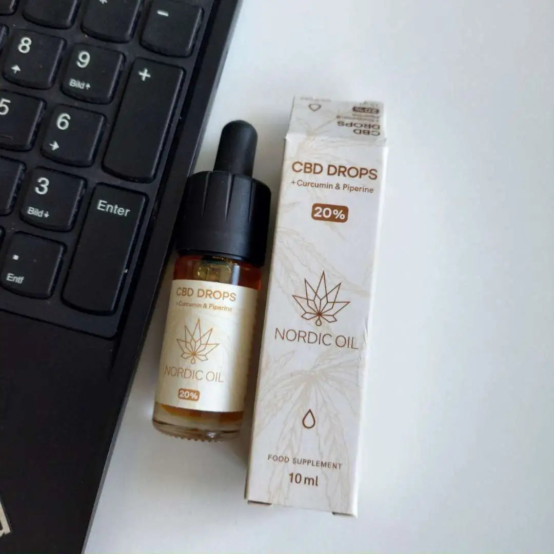 Nordic Oil CBD-drops med pipette og æske, 20% curcumin og piperin ved siden af en computer