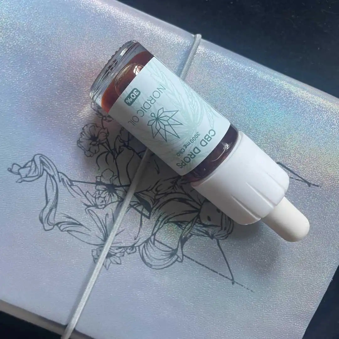 CBD-drops flaske med dropper liggende på sølvglitrende notesbog med blomstertegning