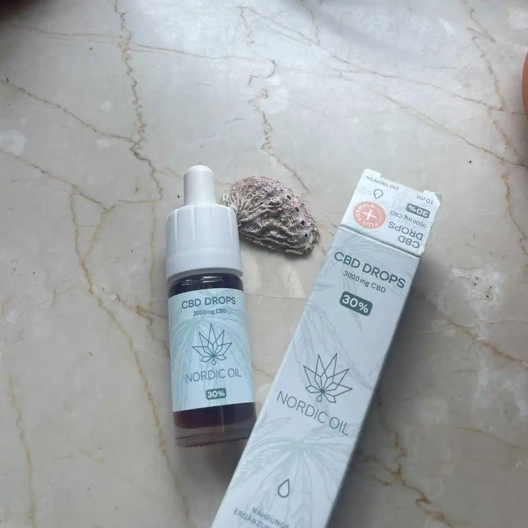 CBD-dråber fra Nordic Oil med æske på marmoroverflade ved siden af en skal.
