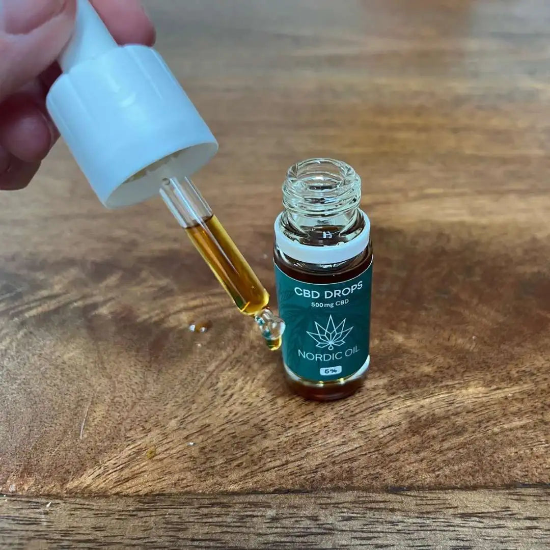 Hånd holder en dropper over en åben flaske CBD-drops fra Nordic Oil