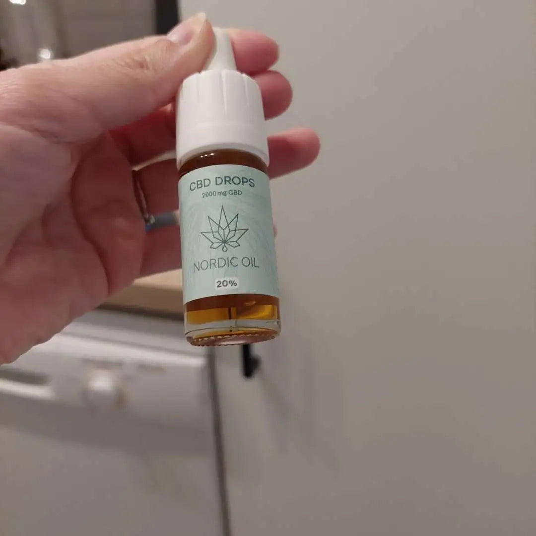 Hånd, der holder en lille CBD-dråberflaske fra Nordic Oil med blå etiket og 2000 mg CBD