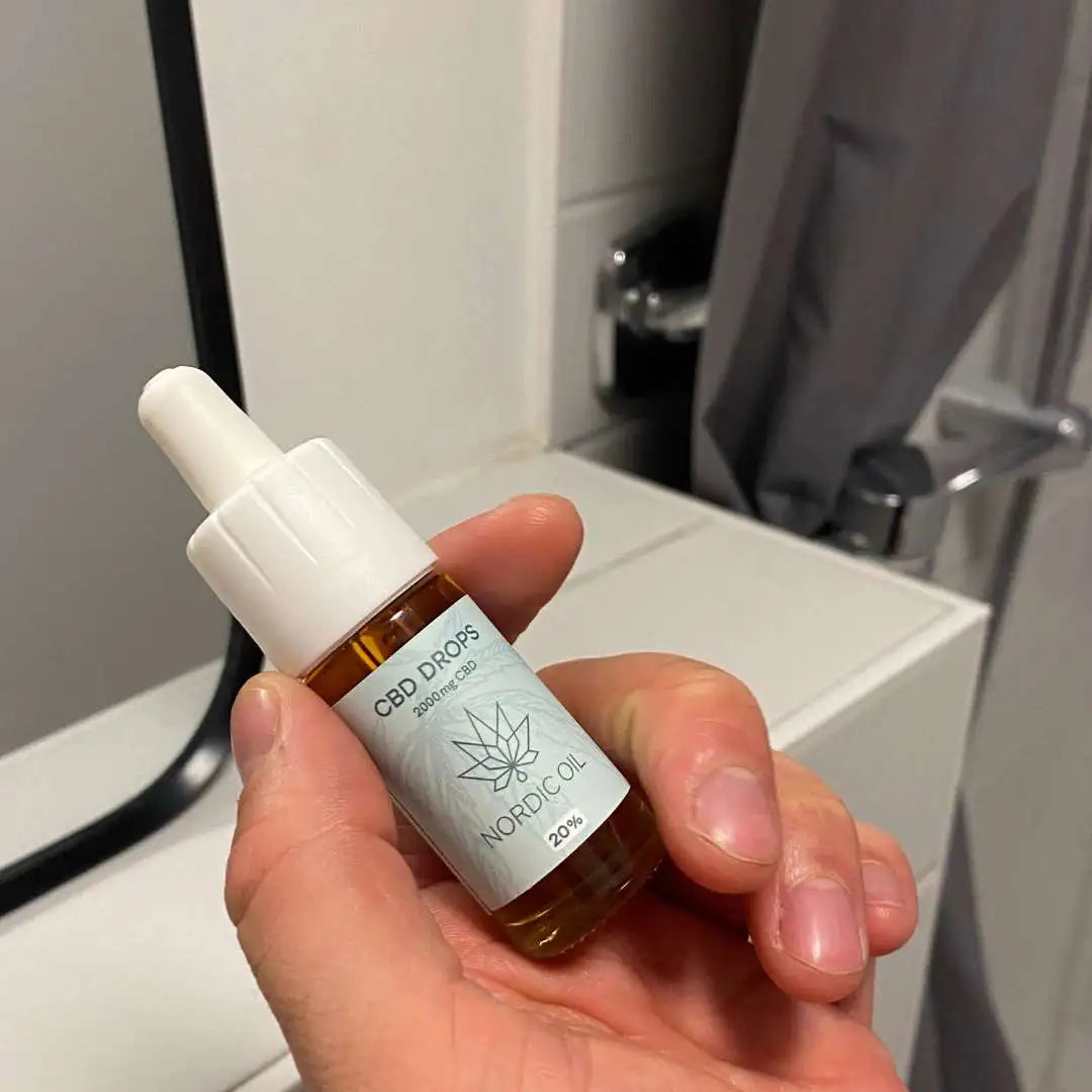 Hånd holder en lille brun glasflaske med dropper til CBD-dråber, mærket Nordic Oil.
