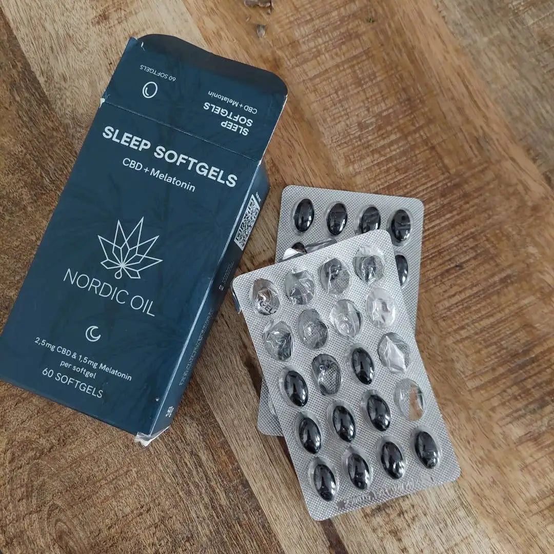 Nordic Oil Sleep Softgels med CBD og melatonin, blisterpakker ved siden af en blå æske på træbord.