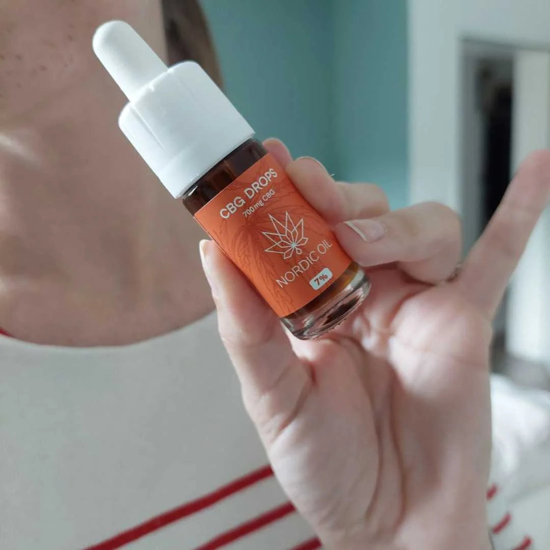 En dropperflaske med CBG Drops Nordic Oil, orange etikette og cannabisblad, holdes af en hånd