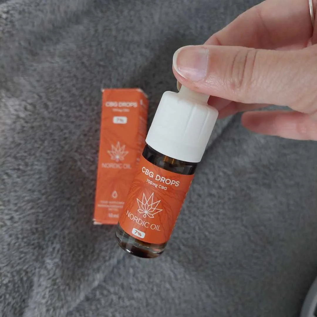 CBD-dråber fra Nordic Oil med orange etikette og dropper, en hånd holder flasken.