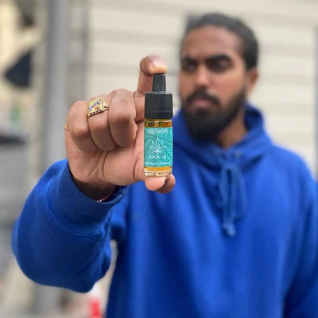 Mand i blå hættetrøje viser en lille flaske CBD-olie med dropper tæt foran kameraet
