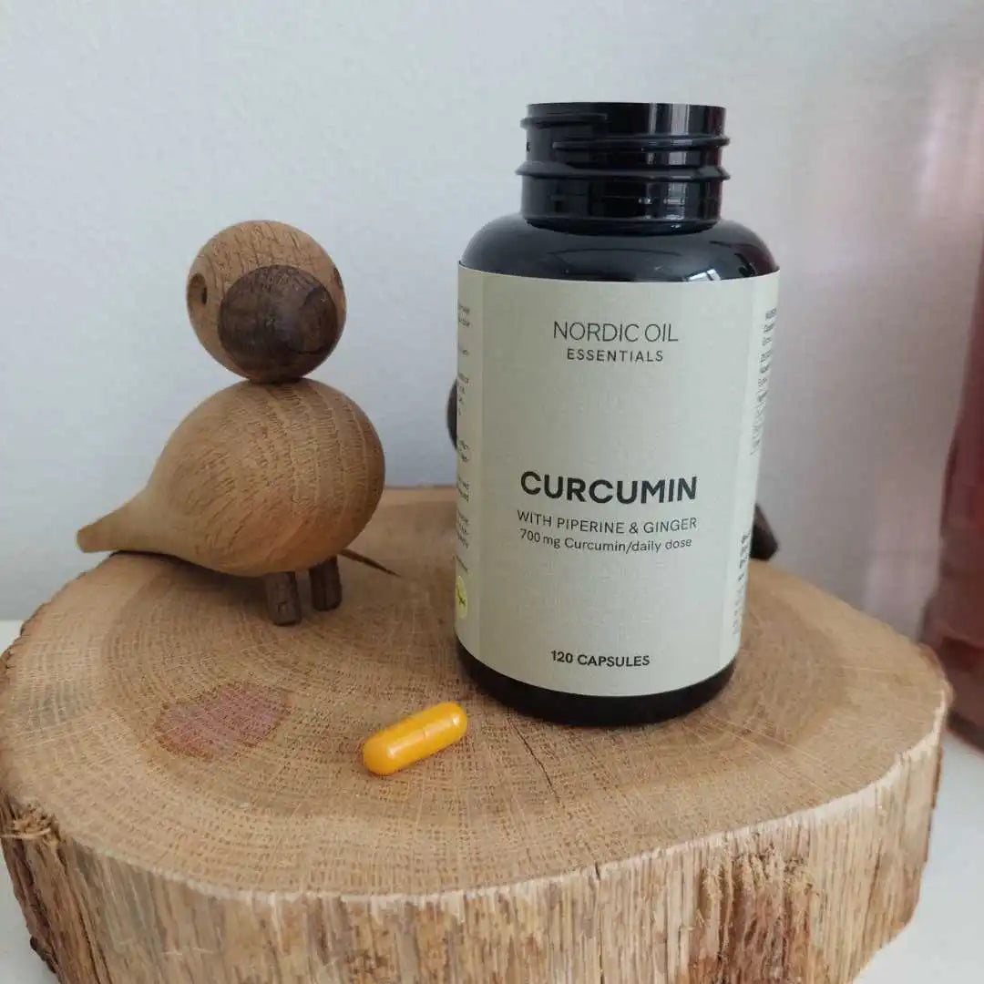Nordic Oil Essentials Curcumin-kosttilskud med piperin og ingefær på en rund træstub, med en lille gul kapsel foran.