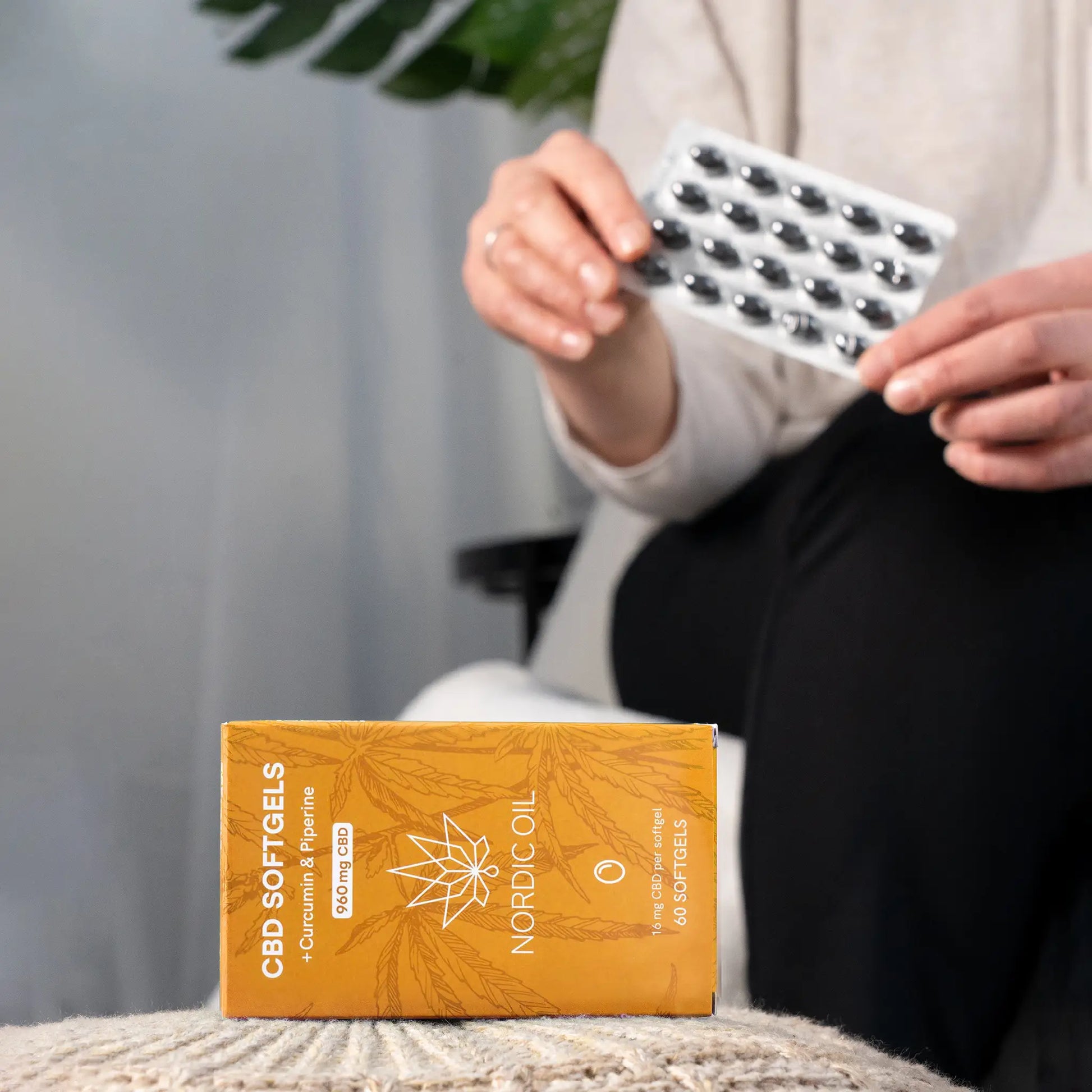 Orange Nordic Oil CBD Softgels-æske med en person, der holder en blisterpakning med kapsler.