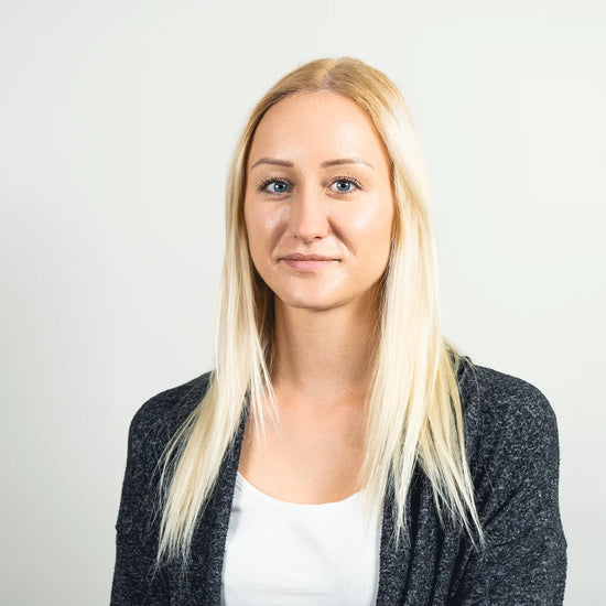 Portrett af en blond kvinde i hvid top og mørk cardigan mod en neutral baggrund.
