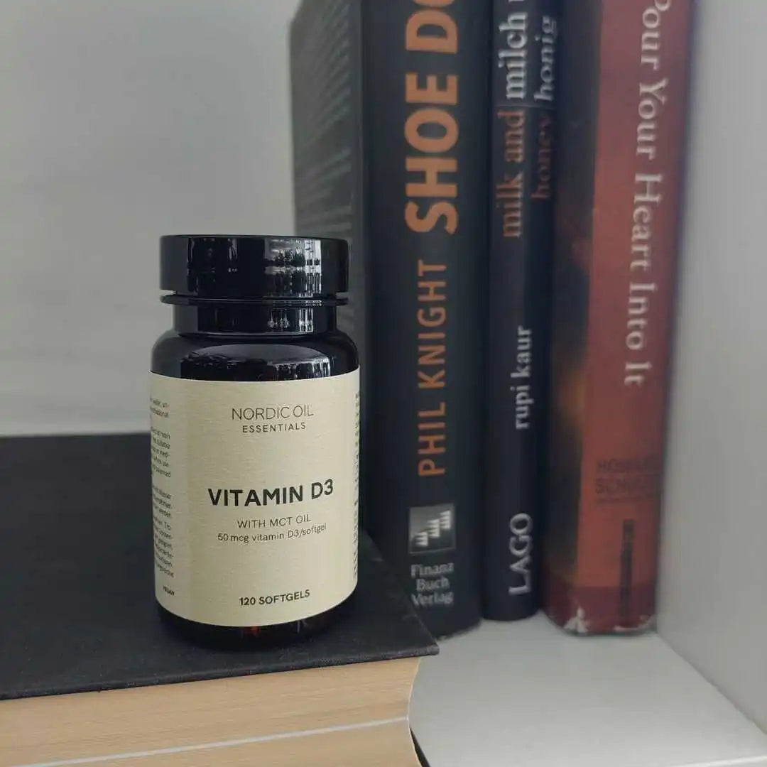 Nordic Oil Essentials Vitamin D3 softgel-flaske ved siden af bøger.