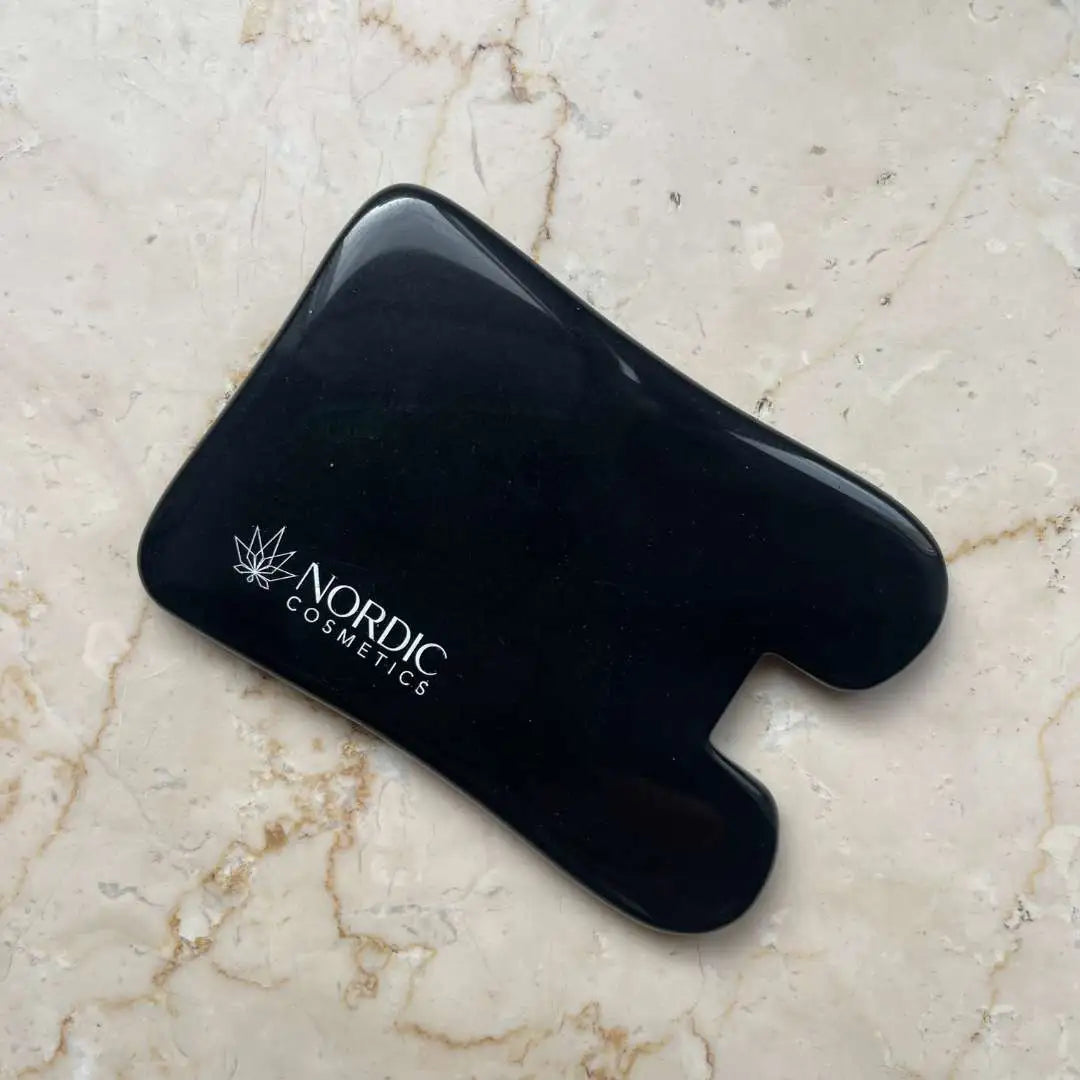 Sort kosmetikredskab med Nordic Cosmetics-logoet på en lys marmoroverflade.