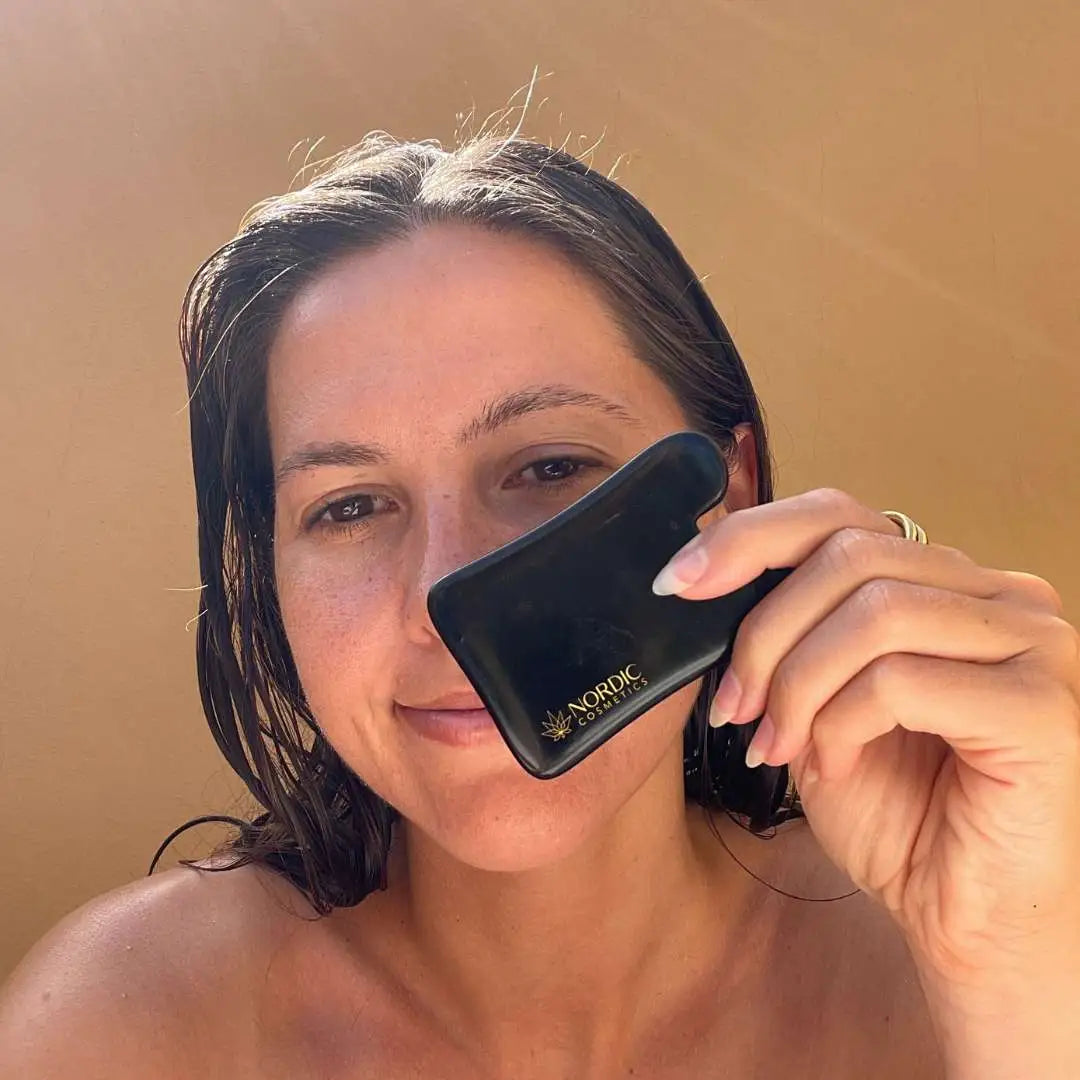 Person holder en sort kosmetikboks med Nordic Cosmetics-logo tæt ved ansigtet.