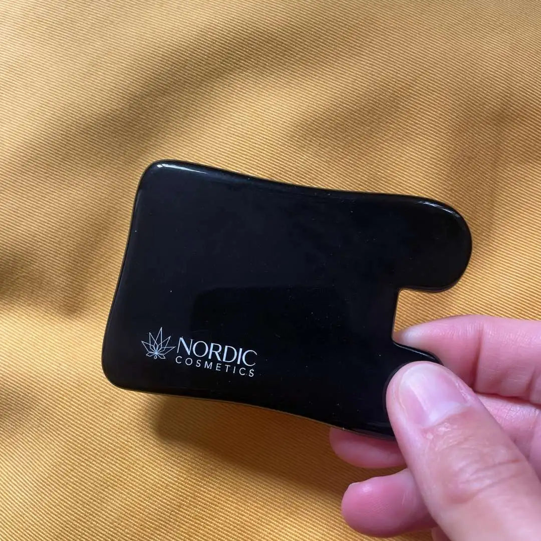 Sort makeup-kompakt med Nordic Cosmetics-logo, holdes af en hånd mod en gylden baggrund.