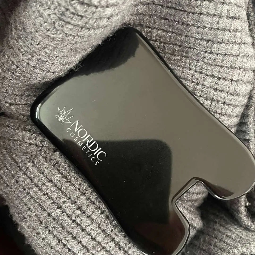 Sort kosmetisk enhed fra Nordic Cosmetics med cannabisblad-logo liggende på gråt strikket stof
