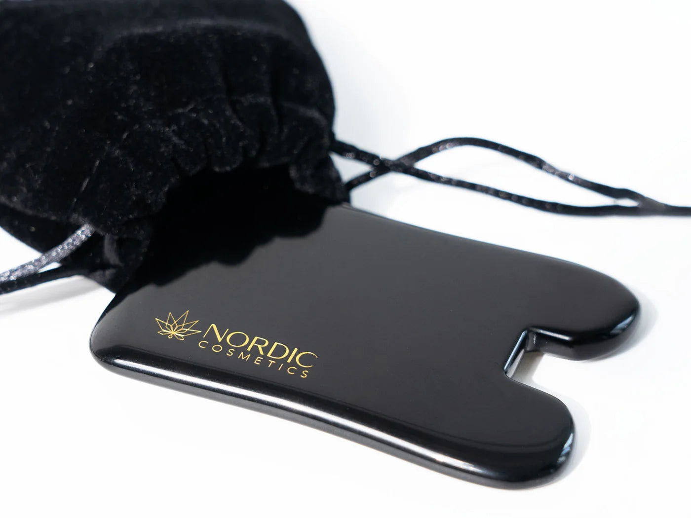 Sort, blank vedhæng med gyldent Nordic Cosmetics-logo og sort snor