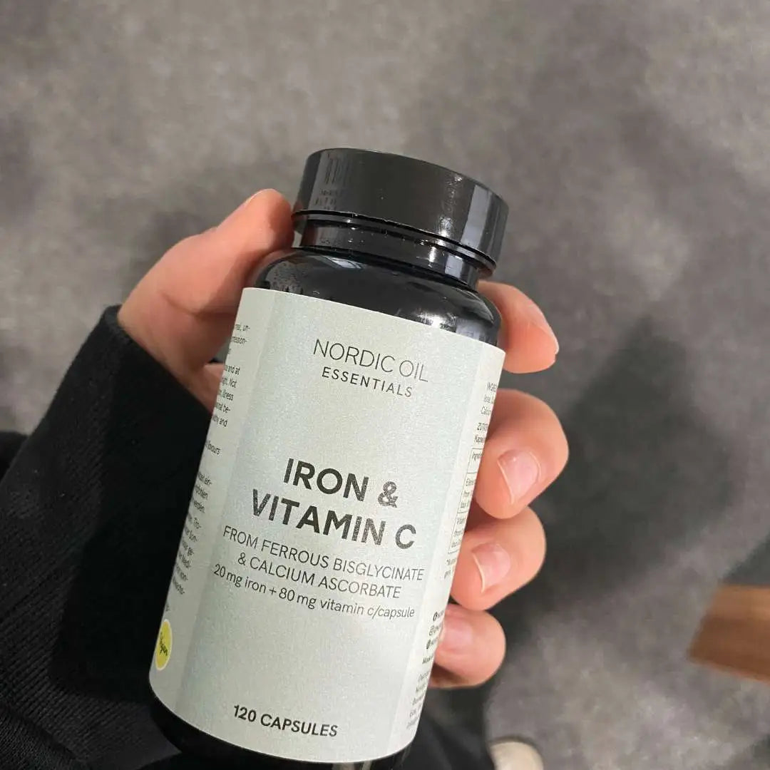 Hånd, der holder en flaske Nordic Oil Essentials Iron & Vitamin C kosttilskud (jern og C-vitamin).