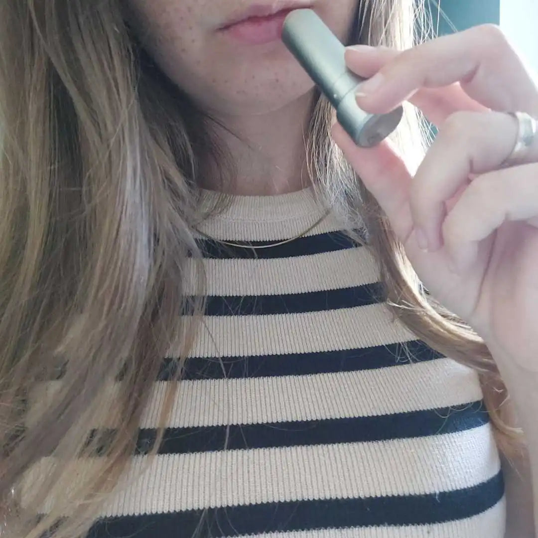 Person holder en sølvfarvet vape pen tæt ved munden.
