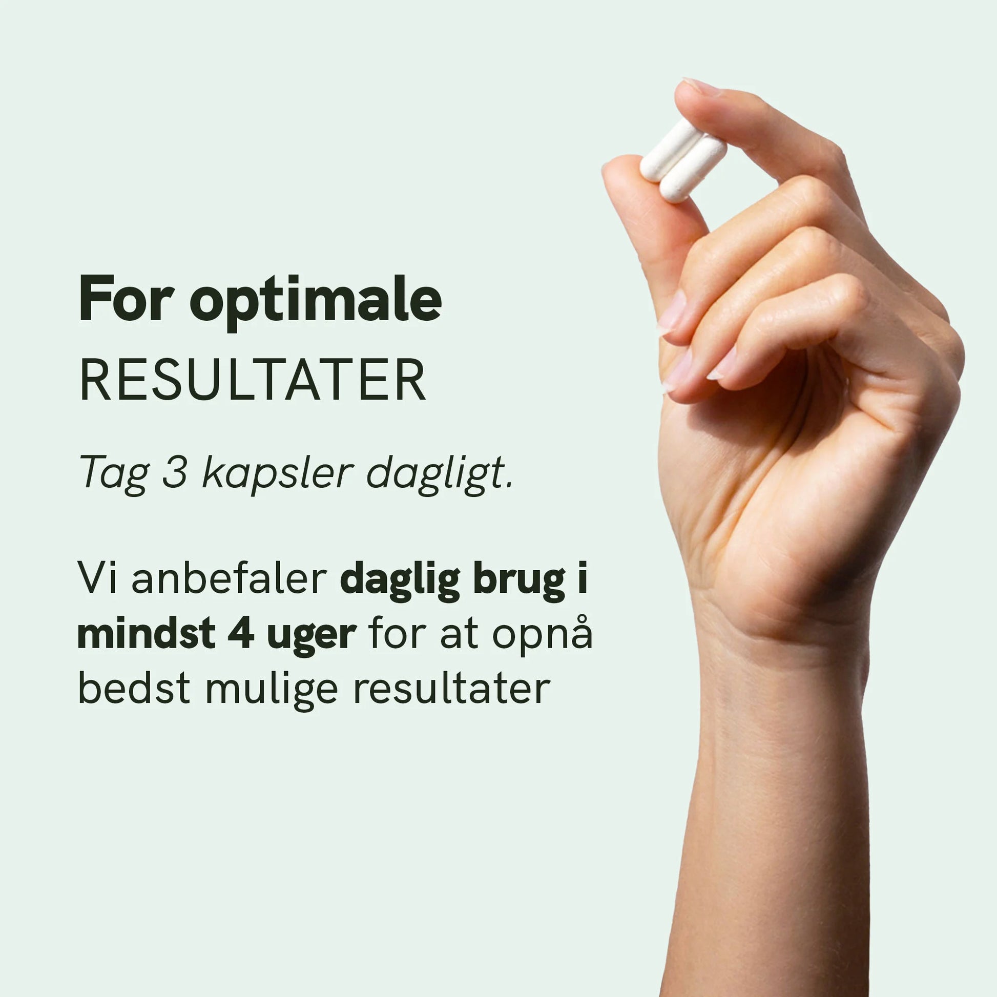 Hånd holder to hvide kapsler mod en lysegrøn baggrund.