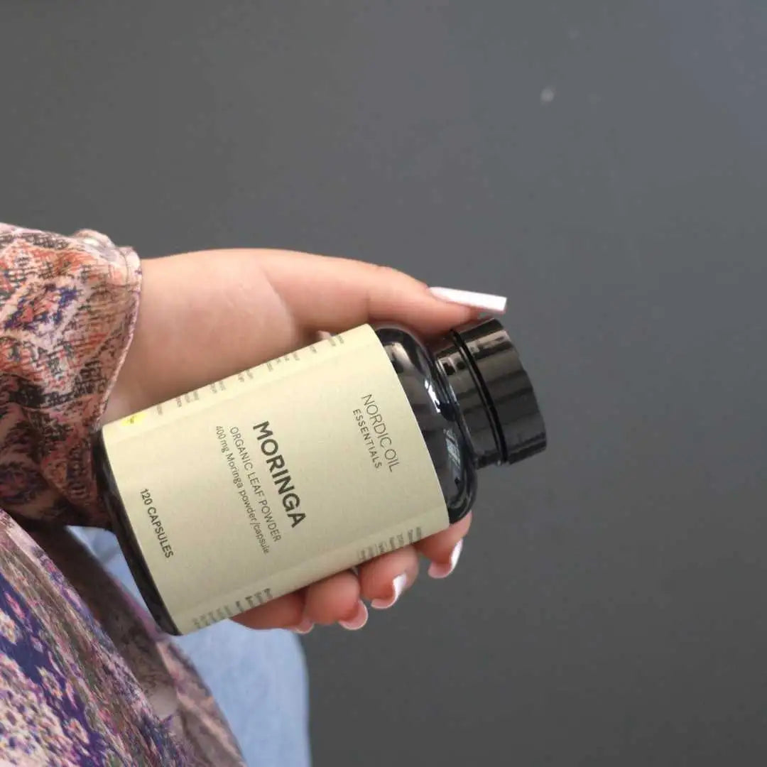 Hånd der holder en Nordic Oil Moringa-tilskudflaske med beige etiket og sort låg.