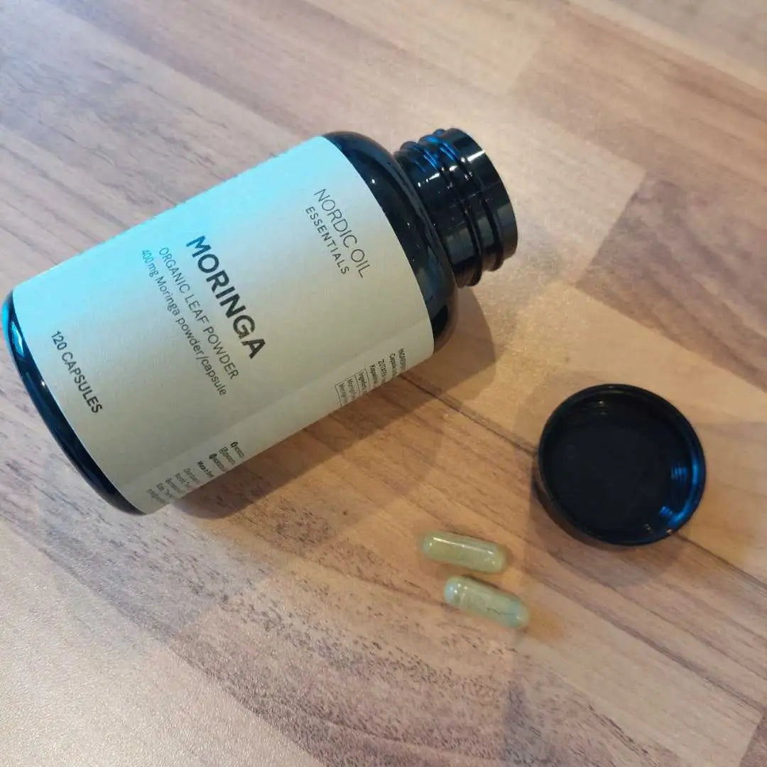 Moringa-kapsler og en åben flaske fra Nordic Oil Essentials på træbord.