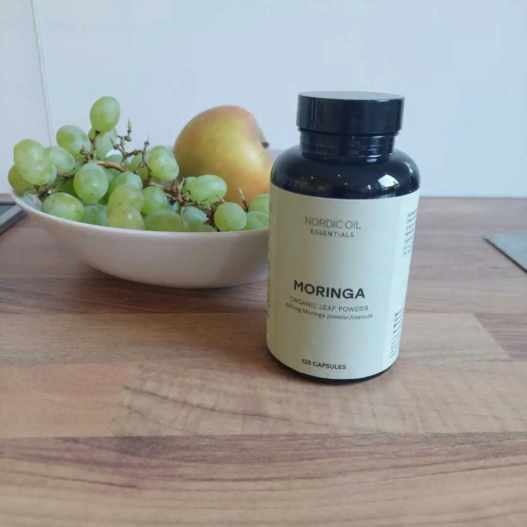 Nordic Oil Essentials Moringa-kapsler på bordet ved siden af en skål med grønne vindruer i baggrunden
