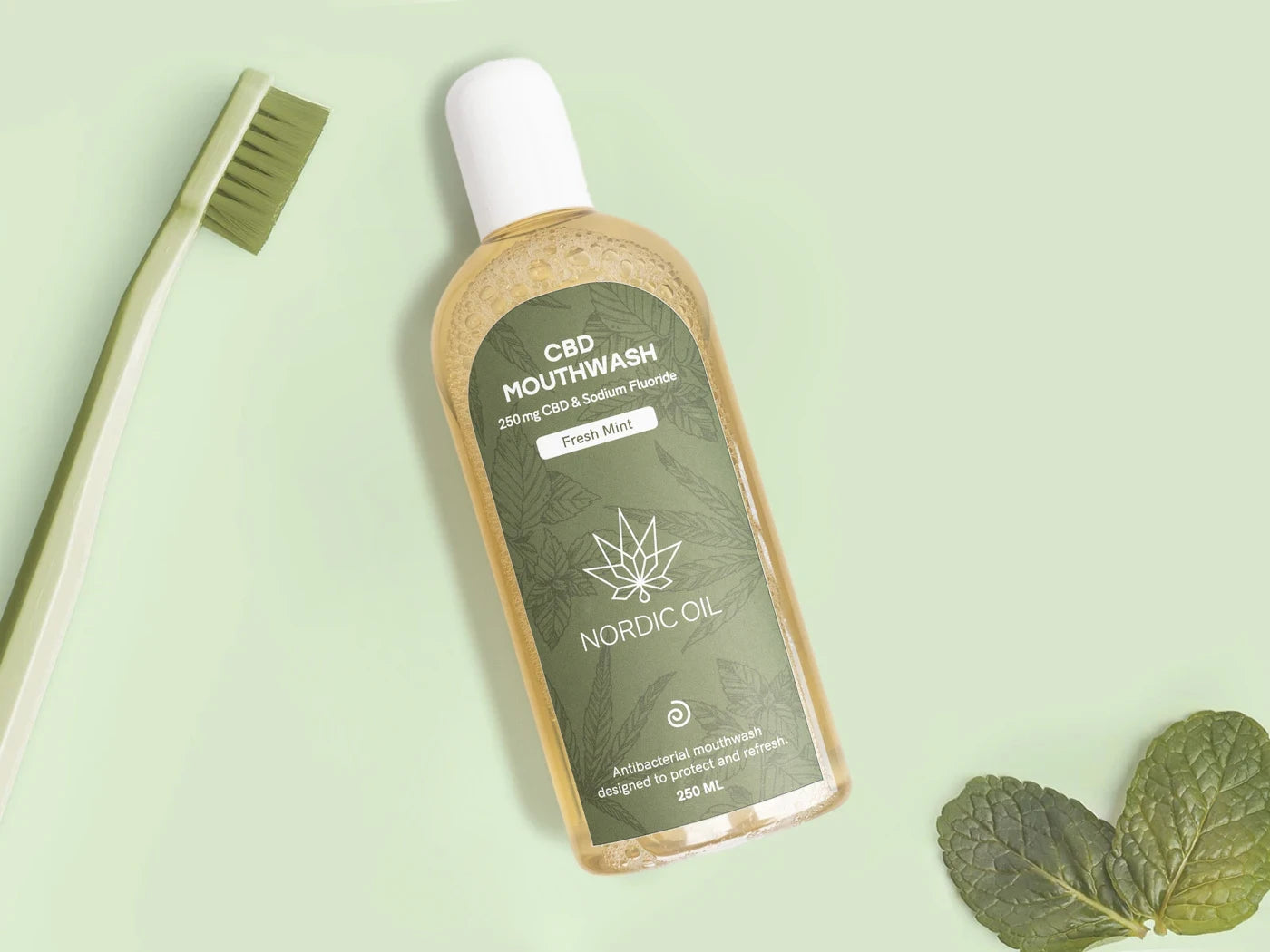 Nordic Oil CBD mundskyllevæske med frisk mynte, ved siden af en tandbørste og mynteblade