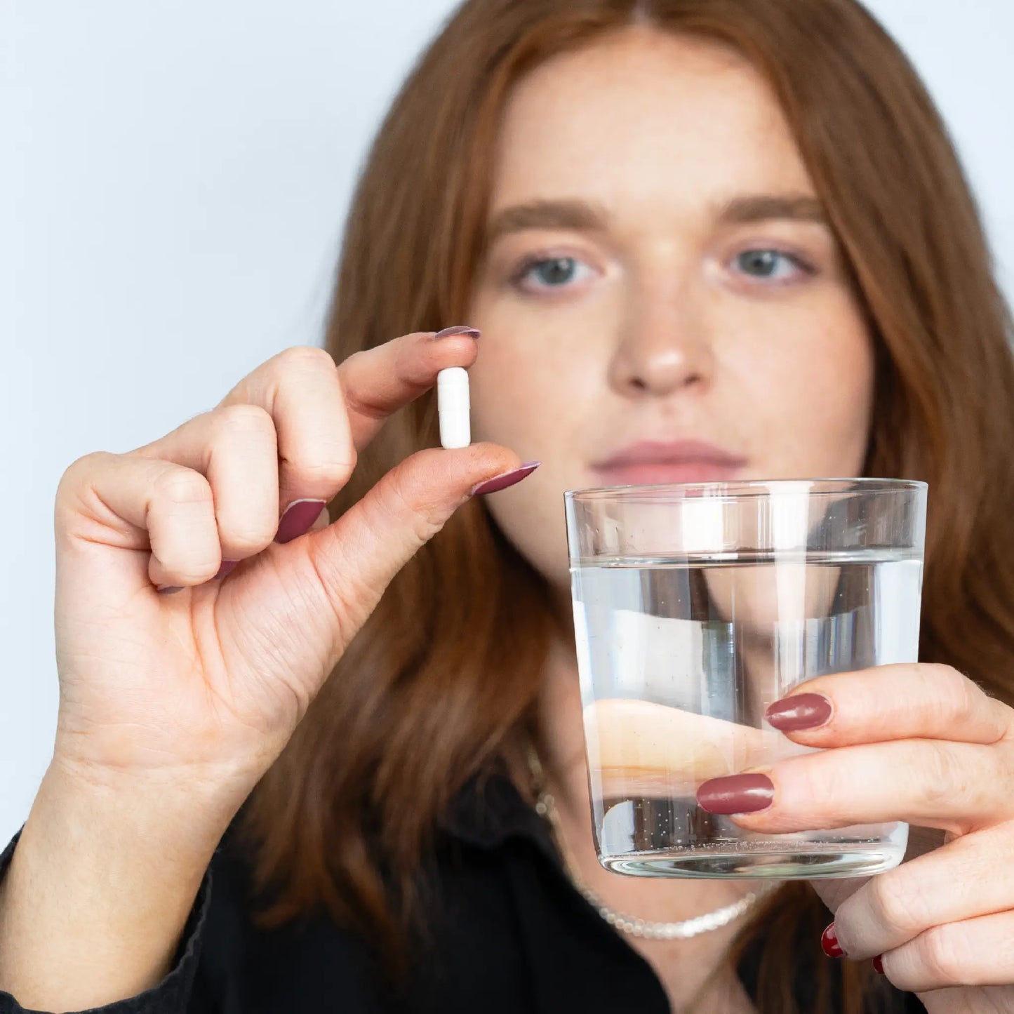Kvinde holder en hvid kapsel mellem fingrene og et glas vand.