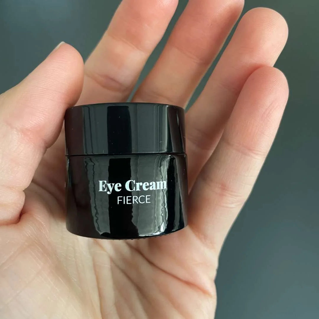 Sort øjencremekrukke mærket Eye Cream Fierce holdes i en hånd.